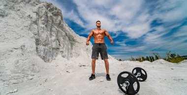 Taş ocağında halterin yanında duran kaslı adam. Taş ocağında duran kaslı bir adam kameraya bakıyor..