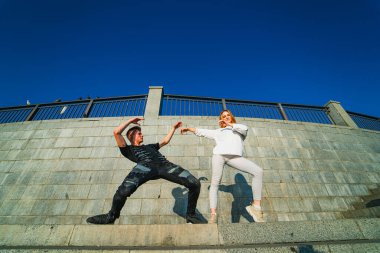 Beton Duvarda Dans Eden Çift. Arka planda mavi gökyüzü olan genç bir çift beton bir duvarda dans ediyor..