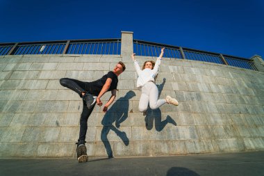 Duvarın önüne atlayan bir çift. Siyahlı bir adam ve beyazlı bir kadın güneşli bir günde mutlu bir şekilde duvarın önüne atlarlar..