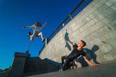 Şehir Merdivenlerinde Akrobatik Dublörlük Yapan Çiftler. Genç bir kadın havada zıplarken, genç bir adam merdivenlerin altında amuda kalkıyor..