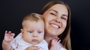 Yeni doğmuş bebeğiyle gülümseyen mutlu anne. Kafkasyalı bir adam ailesine yaklaşıyor. Kapatın. Siyah arkaplan.