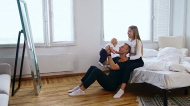 Mutlu ebeveynler küçük çocuklarıyla birlikte yatak odasındalar. Baba oğlunu büyütür ve anne onu yanağından öper..