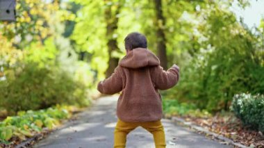 Neşeli bir şekilde dışarı atlayan mutlu bir çocuk. Sonbahar parkında yürüyüş yapan aktif bir bebek. Bulanık arkaplan.