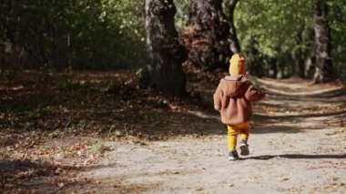 Sıcak kıyafetler giyen bebek parkın yanından geçiyor. Çocuk durur ve şaşkınlıkla kameraya bakar..