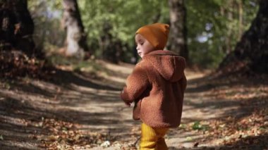 Kahverengi ceketli ve sarı şapkalı sevimli oğlanı takip ediyorum. Sonbahar parkında yürüyüş yapan tatlı çocuk..