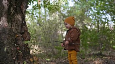 Uzun bir çubuk tutan gülümseyen bebek. Bebek doğada mutlu bir şekilde oynar. Bulanık arkaplan.