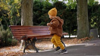 Kahverengi ceketli ve sarı şapkalı sevimli çocuk parkta duruyor. Çocuk sonbaharda yürüyüşe çıkıyor..