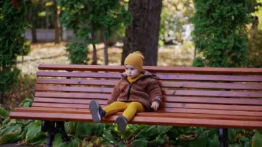 Güzel çocuk bankta oturuyor ve ayağını sallıyor. Sakin ol bebeğim, parkta dinleniyorsun..