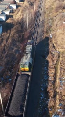 Kargo treni güneşli bir kış gününde demiryolunda. Her iki taraftan birçok garajın arka planında bir yük treninin üst görüntüsü var. Hava görüntüsü. Dikey video