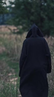 Sahadaki cadının arkadan görünüşü. Kara ölüm, doğanın arka planında yavaş yavaş kaybolur. Dikey video