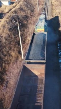 Yük treni kışın hareket eder. Raylardaki bir kargo treninin en üst görüntüsü. Nakliye, demiryolu ve ulaşım konsepti. Hava görüntüsü. Dikey video