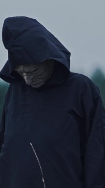 Gizemli karanlık iblis dışarıda. Karanlık kostümlü, bulanık ağaçlı kapüşonlu, korkunç hayalet suratı. Cadılar Bayramı konsepti Dikey video