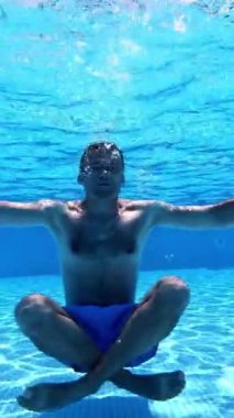 Yoga pozunda suyun altında oturan adam. Yüzme havuzunda egzersiz yapan sağlıklı bir adamın sualtı görüntüsü. Su altı sporu. Dikey video