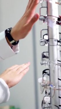Görme konsepti. Optik mağazasında şık gözlüklü bir kadın var. Alıcı dükkandan yeni gözlük seçiyor. Dikey video