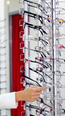 Optik dükkanındaki kadın alıcının yan görüntüsü. Genç ve güzel bir kadın yeni gözlük seçiyor. Sağlık sigortası konsepti. Dikey video