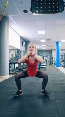 Genç bayan spor salonunda çömeliyor. Çekici kız spor salonunda günlük egzersizini yapıyor. Sağlıklı bir yaşam tarzı. Dikey video