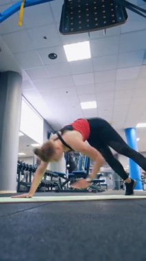 Spor salonunda spor antrenmanı. Spor takım elbiseli genç bir kadın modern fitness kulübünde paspasın üzerinde egzersiz yapıyor. Dikey video