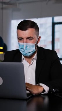 Maskeli bir iş adamı dizüstü bilgisayarın önünde oturur. Adam dikkatlice ekrana bakıyor, bir şeyler yazıyor ve konuşuyor. Dikey video