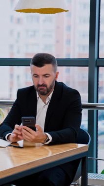 Sakallı adam akıllı telefonunun ekranına bakıyor. İş adamı bilgi aramak ve alet kullanmak konusunda endişeli görünüyor. Dikey video
