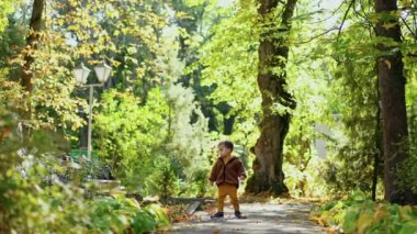 Kahverengi ceketli küçük çocuk parktaymış. Kameraya doğru koşan sevimli bir bebek. Güneşli gün arkaplanı.