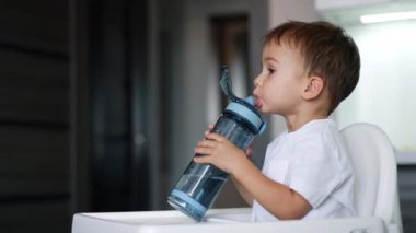 Spor şişesinden su içen sevimli bir çocuk. Tatlı çocuk kameraya bakıyor, gülüyor ve şişe kapağını kapatıyor..