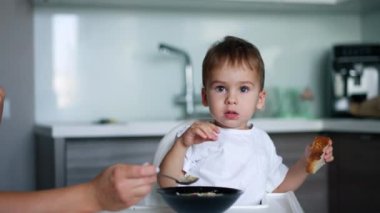 Küçük çocuk çorba içmeyi reddediyor. Güzel bir bebek elinde bir parça ekmek tutarak annesinin elinde kaşıktan kaçıyor..