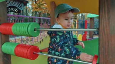 Güzel beyaz çocuk oyun bahçesinde abaküsle oynuyor. Erkek çocuk sonbaharda dışarıda iyi vakit geçiriyor..