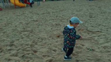 Sevimli beyaz çocuk sonbaharda oyun bahçesinde olacak. Çocuk bankın yanına koşar ve üzerine biner..