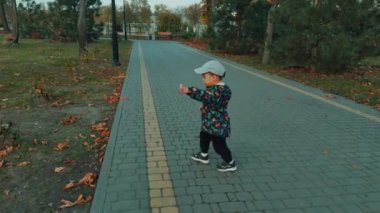 Tatlı beyaz çocuk sonbahar parkının yanından geçiyor. Küçük çocuk ellerin büyük heykelini fark eder ve onlara dokunmaya gelir..