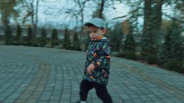 Şapka, ceket ve pantolon giyen şirin küçük çocuk dışarıda yürüyor. Bebeğim sonbahar parkında vakit geçiriyor..