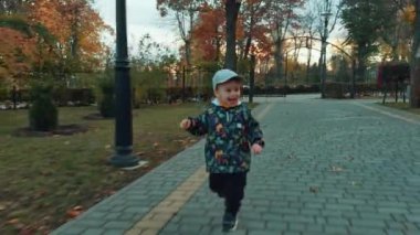 Parkta koşuşturan neşeli enerjik çocuk. Sonbaharda yürüyüş sırasında aktif zaman geçiren sevimli gülümseyen bebek..