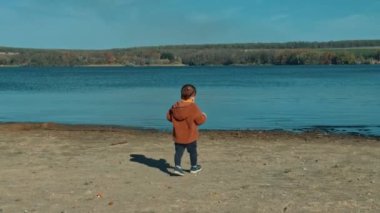 Kahverengi ceketli bir çocuğun nehre doğru yürüdüğünü gördüm. Bebek suya taş atıyor ve yenilerini arıyor..