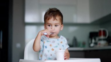 Düşünceli çocuk, elinde kaşıkla oturuyor. Bebek yoğurdunu yavaş yavaş yiyor. Bulanık arkaplan.