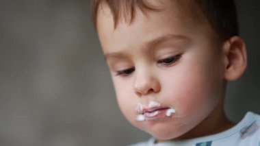 Yoğurt yiyen güzel bir beyaz çocuğun yüzü. Çocuğun yüzü süt ürünlerine bulaşmış. Kapat..