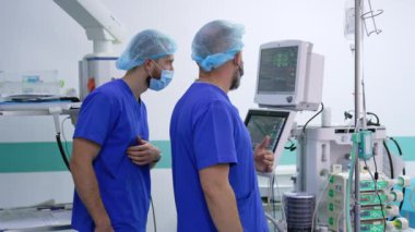 Üniformalı iki orta yaşlı erkek doktor teçhizatın önünde duruyor. Doktorlar hastanın yaşam sinyallerini monitörde tartışıyor. Modern ameliyathane arka planı.