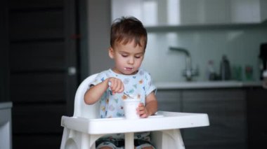 Güzel bir çocuk mutfakta yüksek bir sandalyede oturuyor. Kafkasyalı erkek bebek yoğurt yiyor..