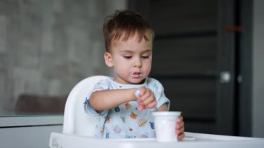 Güzel beyaz bebek mutfakta oturup fincandan yoğurt yiyor. Bebek sağlıklı bir şeyler yiyor..