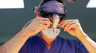 Nöroşirürjiden önce beyaz bir erkek doktor cihaz gözlüğü takıyor. Cerrah, cihazı operasyonda kullanması için ayarlıyor. Kapat..