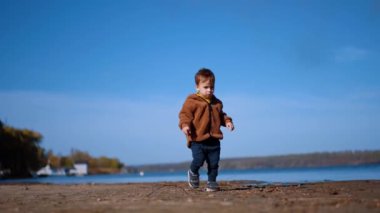 Şirin çocuk taşları aramak için rıhtımın yanından geçiyor. Küçük çocuk bir dala dokunur ve sonra devam eder. Düşük açı görünümü.