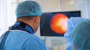 Röntgen koruyucu tasma takan bir cerrahın arka görüntüsü. Ekrana bakıp endoskopi yapan bir doktor. Bulanık arkaplan.