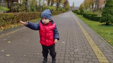 Beyaz, sevimli, sıcacık elbiseli bir çocuk parkta yürüyor. Sonbaharda açık hava.