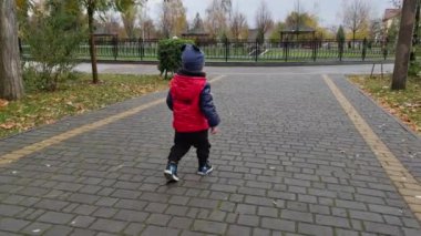 Arka tarafta kırmızı ceketli bir çocuk sokakta yürürken görülüyor. Sonbaharda temiz havada tatlı bir çocuk..