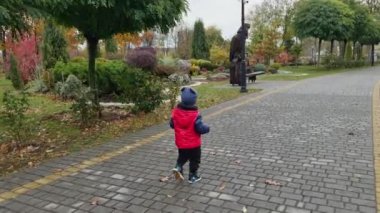 Kalın giysiler giymiş bir çocuğun arkasında yürümek. Küçük çocuk sonbaharda güzel bir parkta..