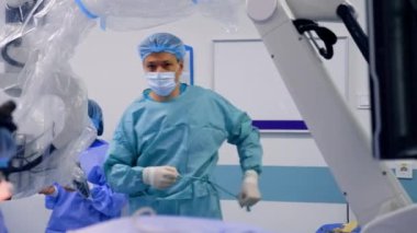 Doktor bornozu bağlar ve ameliyat masasına gelir. Cihaz gözlüklü beyin cerrahı zaten hastaya bakıyor..