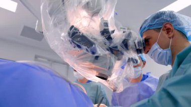 Doktorlar ameliyat sırasında plastik kaplı mikroskoba bakarlar. Hastanedeki modern nörolojik operasyon. Düşük açı görünümü.