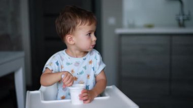 Sakin, sessiz bir çocuk yüksek sandalyede oturuyor elinde bir kaşık, yana bakıyor. Tatlı çocuk yoğurt yiyor..