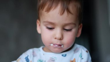 Ağzında süt ürünleri olan sevimli bir erkek bebek. Kaşıkla yoğurt yiyen bir çocuğun yüzü. Kapat..