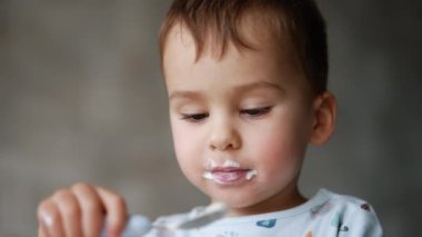 Güzel beyaz bebek lezzetli yoğurdun tadını çıkarıyor. Ağzının her tarafında süt ürünleri olan şirin bir çocuk portresi. Kapat..