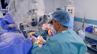 Beyaz erkek cerrahlar ameliyatı gerçekleştiren mikroskoba bakarlar. Hastanede modern mikro cerrahi.