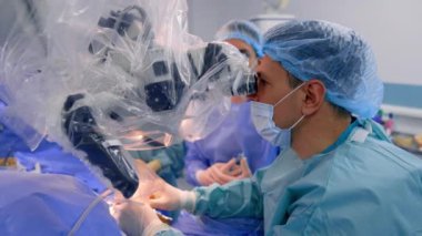 Mikroskoba odaklanmış bir cerrah meslektaşlarıyla konuşuyor. Modern cerrahi odasında beyin cerrahisi.